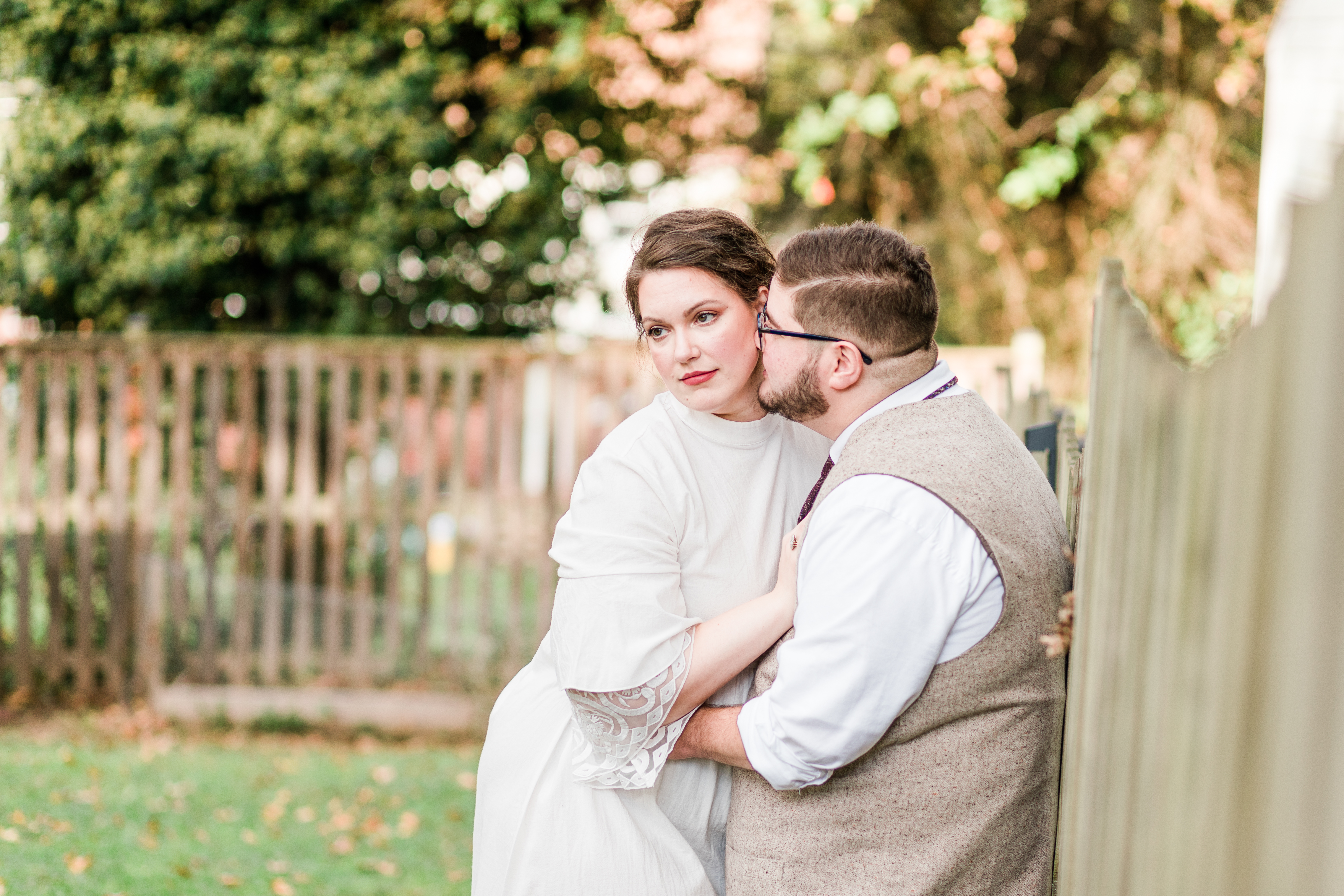 A bride cuddles against her groom next to a fence in her backyard