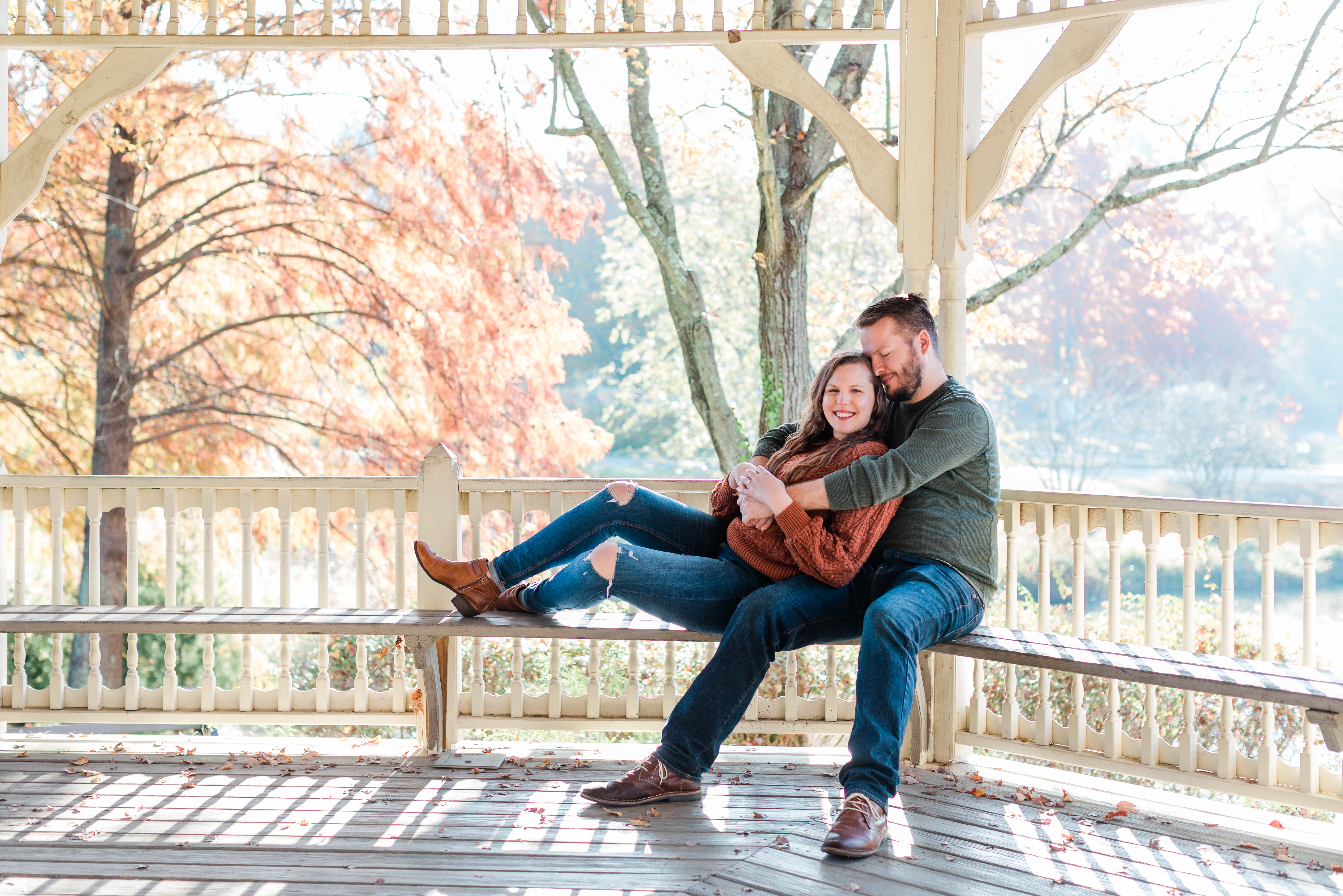 A couple in cozy fall sweaters snuggle on a bench inside a gazebo on a gorgeous fall morning