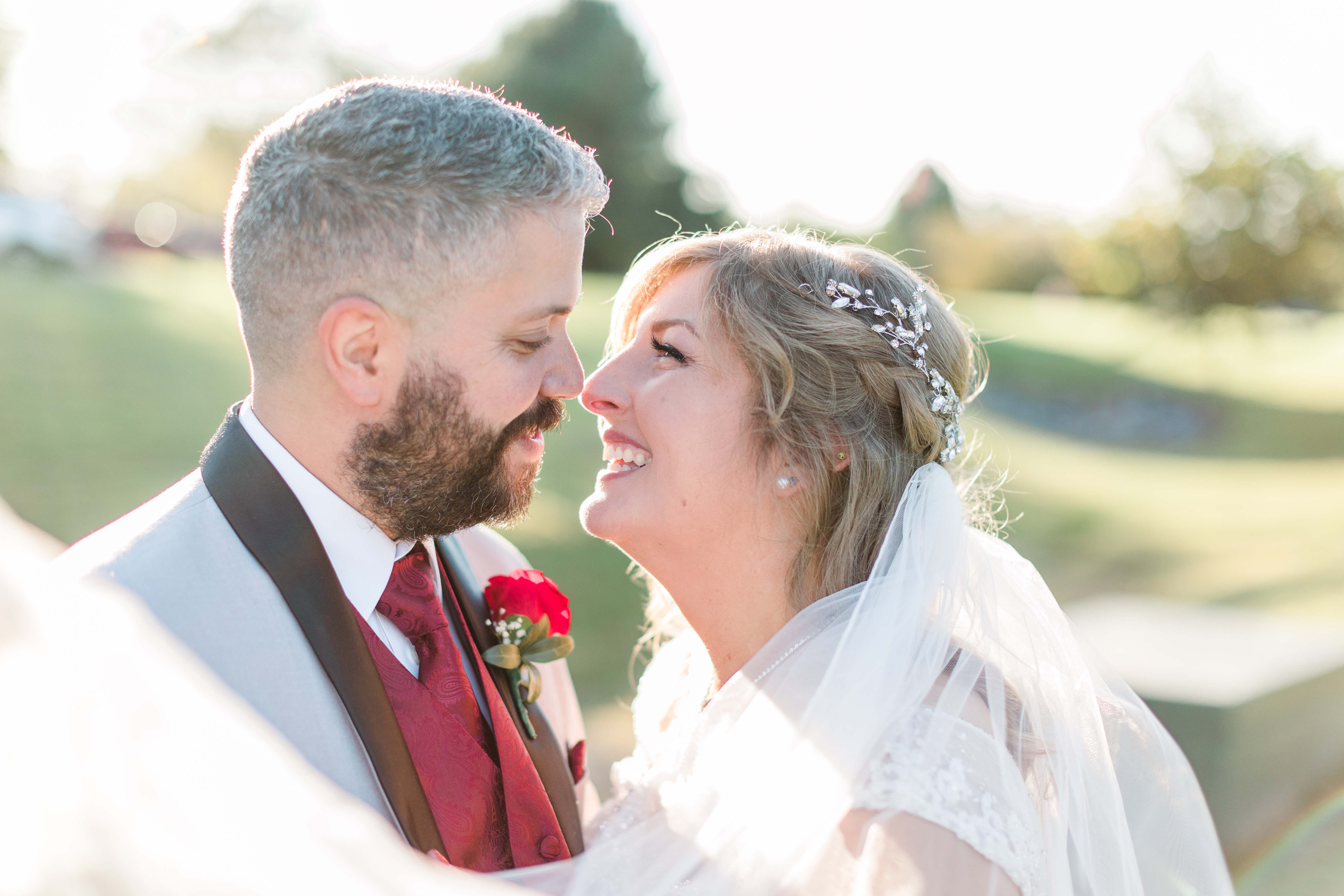 A bride and groom smile at each other, noses almost touching while the veil floats around them