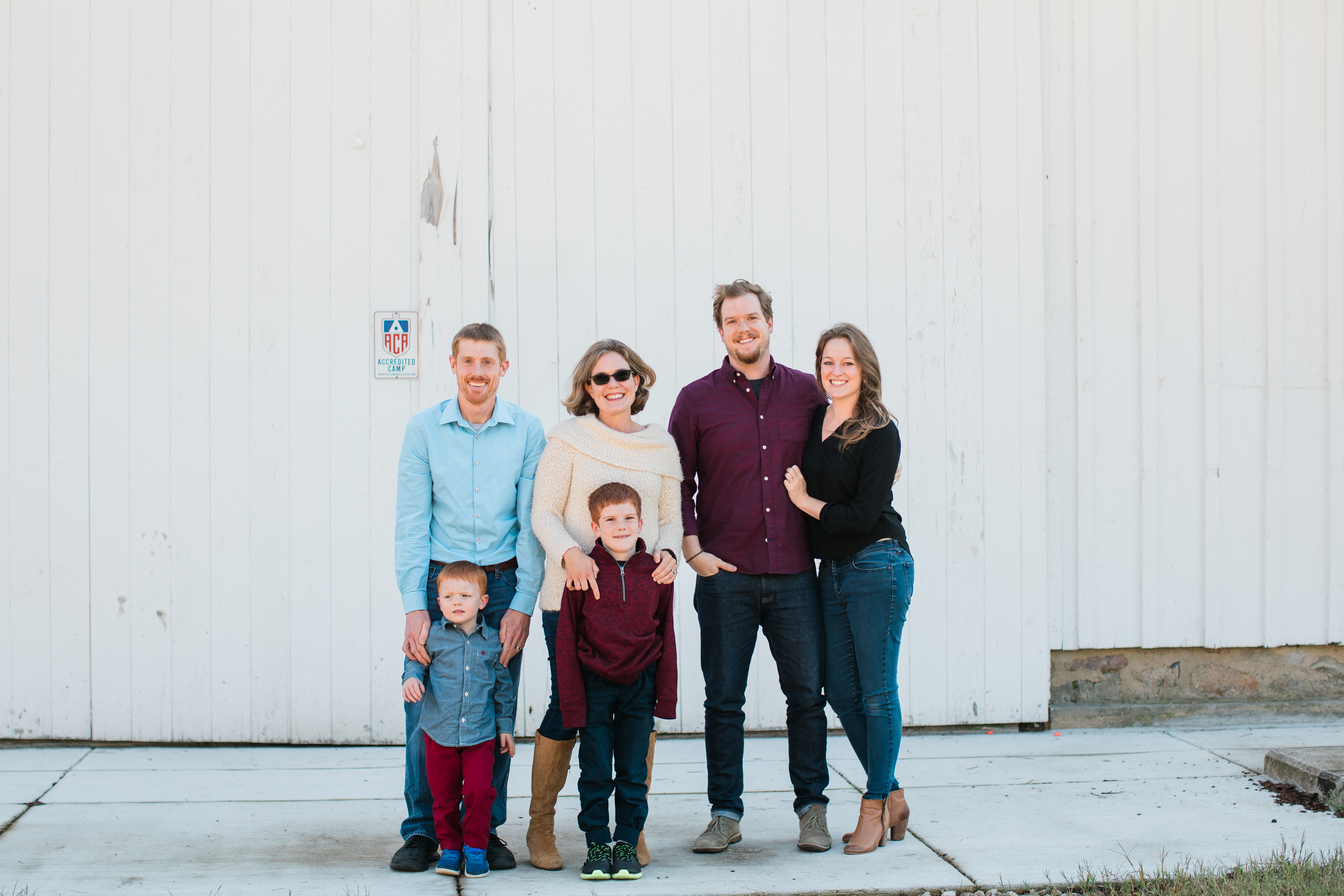 An extended family stand against a white barn and smile at the camera
