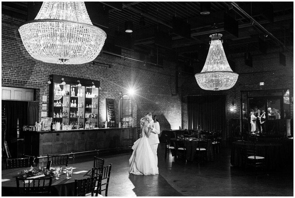 Black and white capture of naval officer and bride sharing private last dance at Union Mills Public House in Frederick. Crystal chandeliers and historic brick walls frame intimate moment at empty reception venue