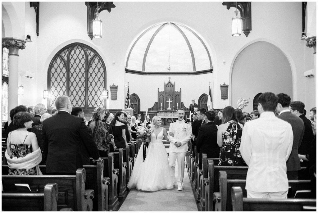 Timeless black and white image of naval officer and bride during recessional in historic Frederick cathedral with vaulted ceiling