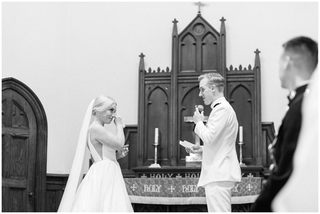 Candid moment during vow exchange at historic cathedral wedding, featuring naval officer in dress whites and bride wiping happy tears