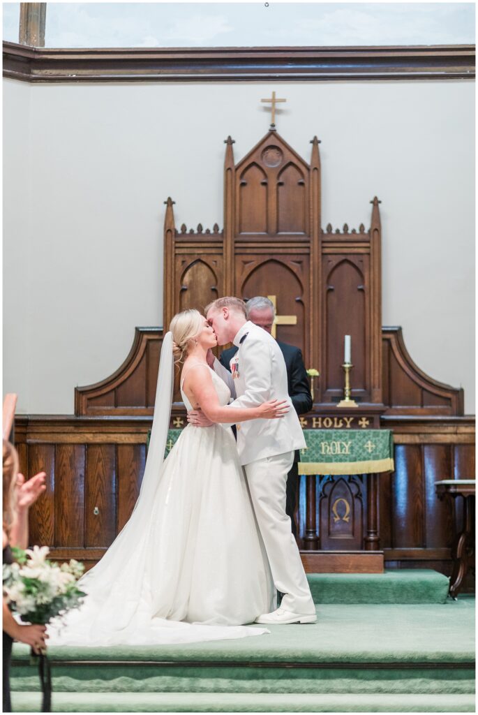 Naval officer and bride share first kiss at altar in historic Frederick church with Gothic wooden details and traditional altar decor