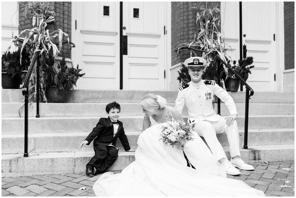 Naval officer and bride share candid moment with ring bearer on historic church steps in downtown Frederick