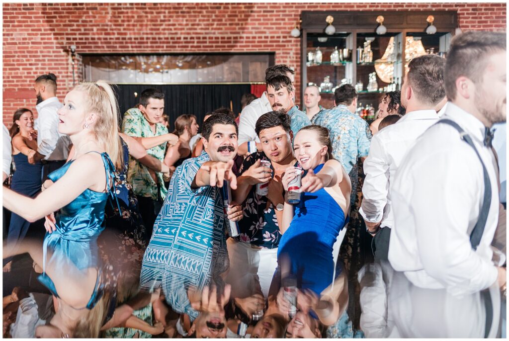 Candid moments from wedding reception dance floor showing guests laughing and celebrating. Mix of formal attire and casual Hawaiian shirts as military wedding transitions to party atmosphere.