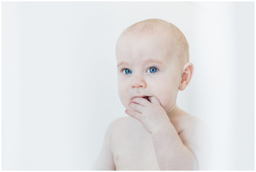 Six-month-old baby with blue eyes looking at camera during milestone photo session in Maryland, captured in a natural light lifestyle portrait.