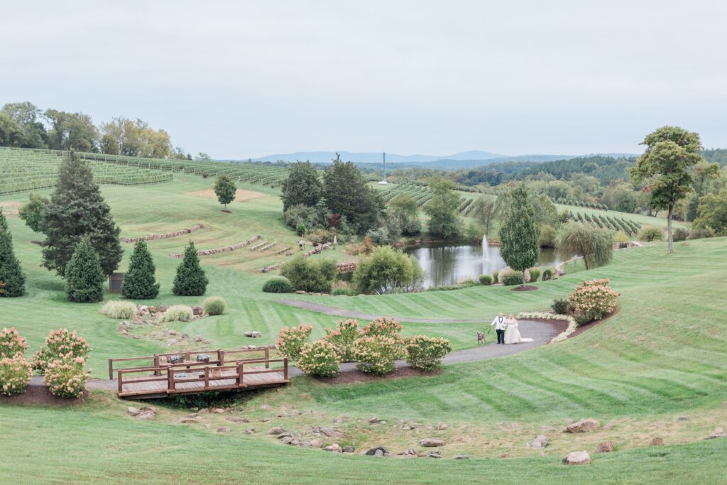 Bride and groom walk up a rolling hill, overlooking a pond during their Stone Tower Winery Wedding