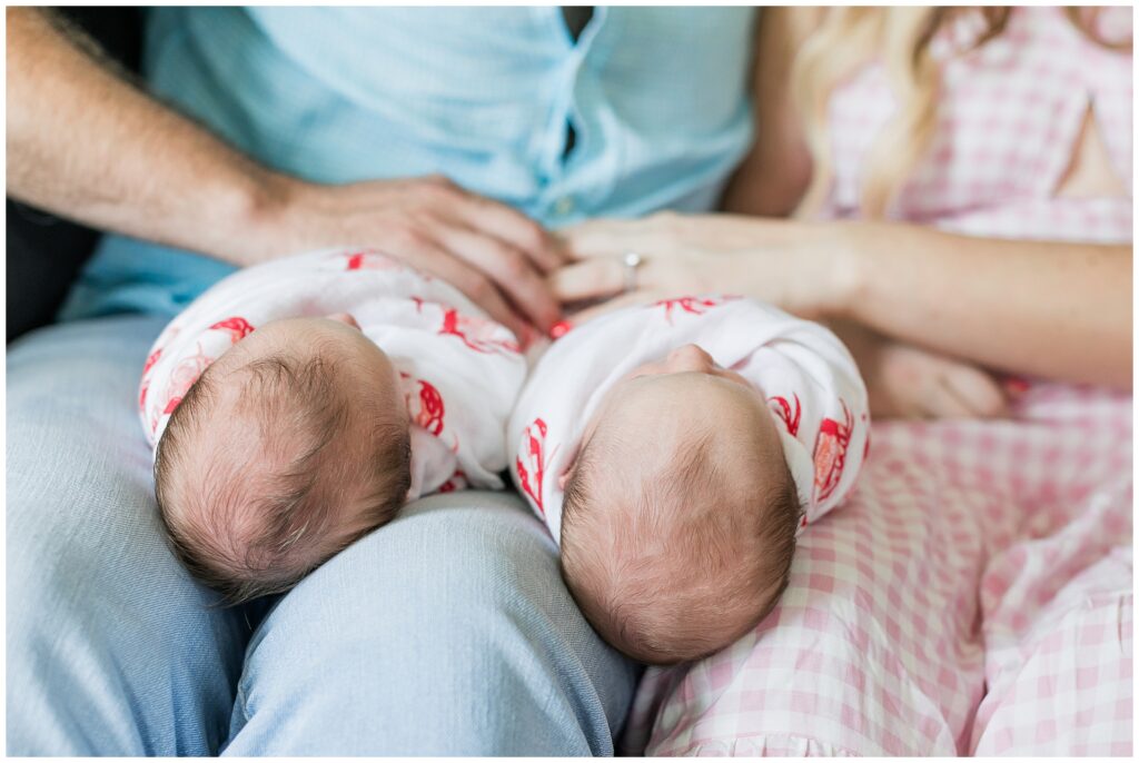 Newborn twins rest on their parents’ laps during a lifestyle newborn photo session in Gaithersburg, MD.