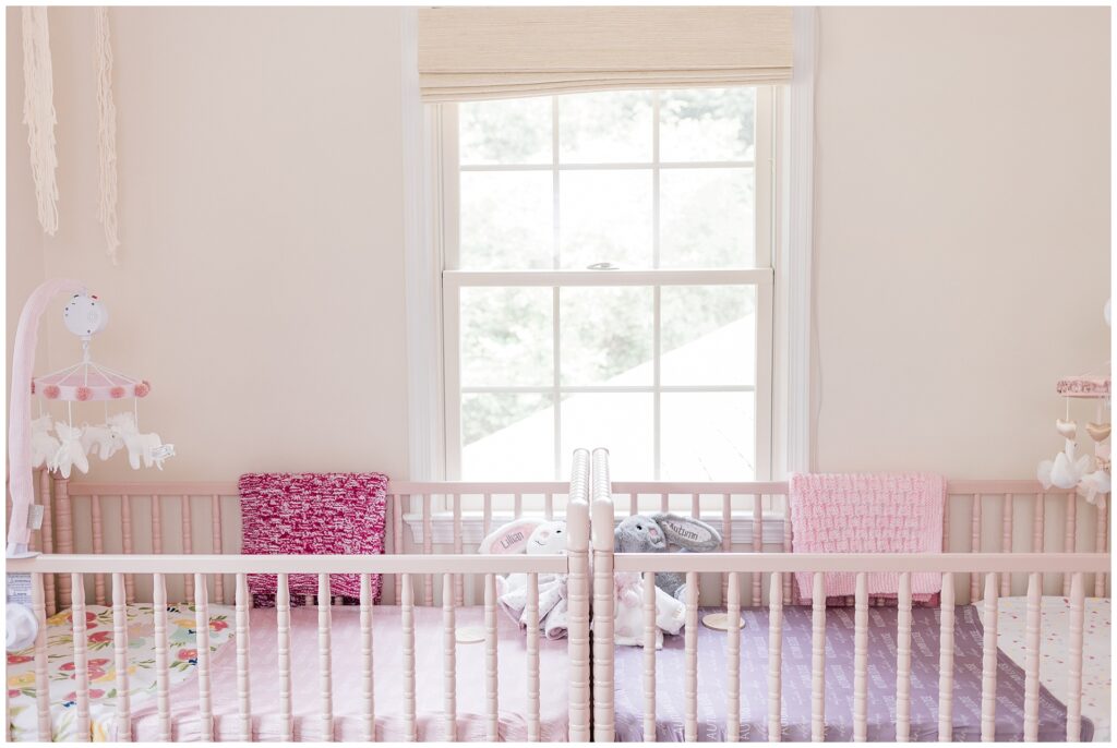 Twin nursery with pink cribs and personalized name pillows during an in-home newborn session in Gaithersburg, Maryland.