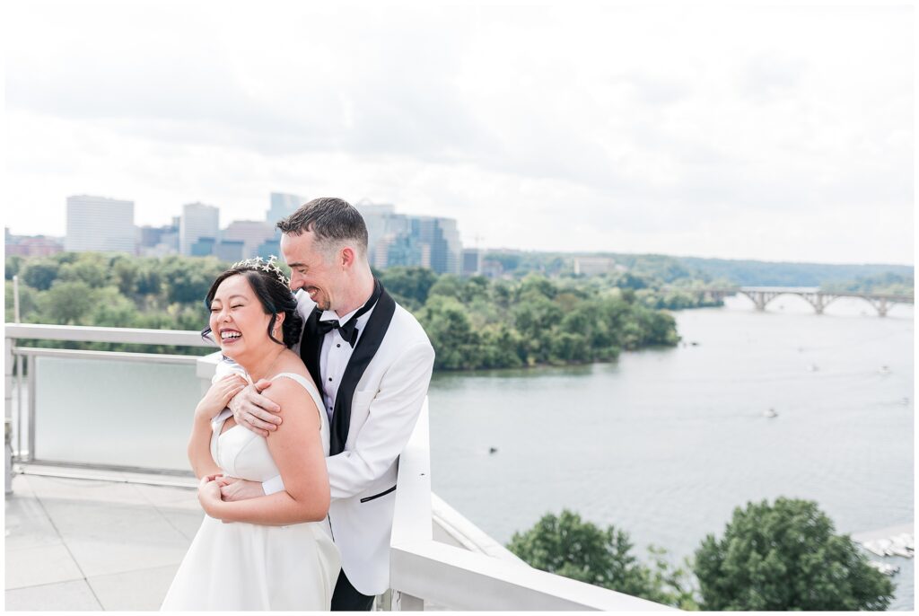Joyful rooftop portrait of bride and groom at The Watergate Hotel overlooking the Potomac River, captured during full-day DC wedding photography coverage.
