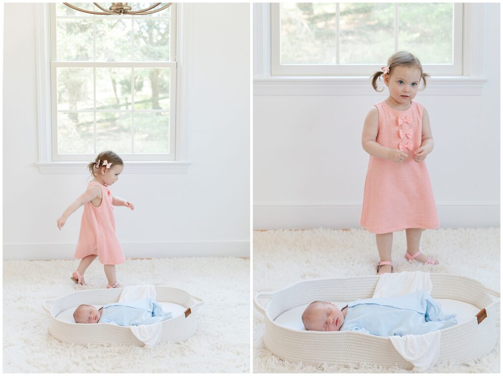 A toddler in a coral pink dress stands beside her newborn sibling in a cream basket, highlighting how coordinating without matching works beautifully in natural-light family portraits.