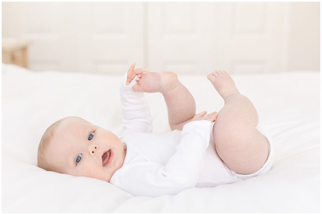 Six-month-old baby wearing white onesie in clean, neutral milestone portrait at home