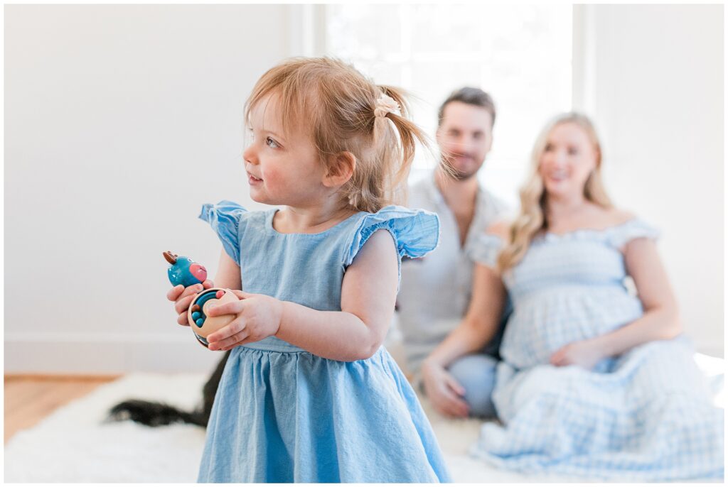 Parents with their twin toddler daughters during an in-home maternity session in Montgomery County, Maryland, celebrating the upcoming arrival of their baby boy.