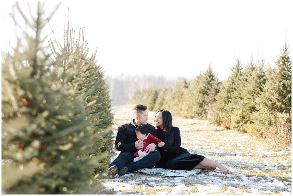 Family photographed together at a Christmas tree farm in Frederick Maryland during a holiday portrait session. These Christmas tree family photos capture a timeless winter setting with natural evergreens.