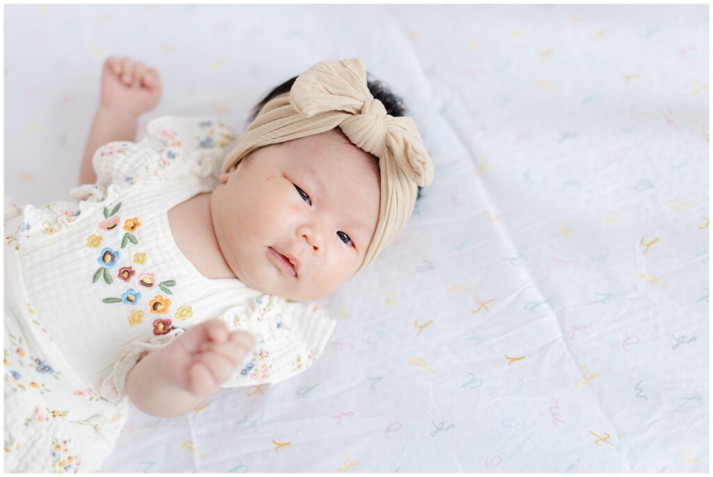 Awake newborn wearing bow headband and floral outfit photographed during an in-home newborn session in Ashburn Virginia