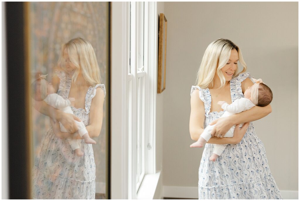 Mother in a white and blue floral dress cradles her baby girl in their newborn home session.