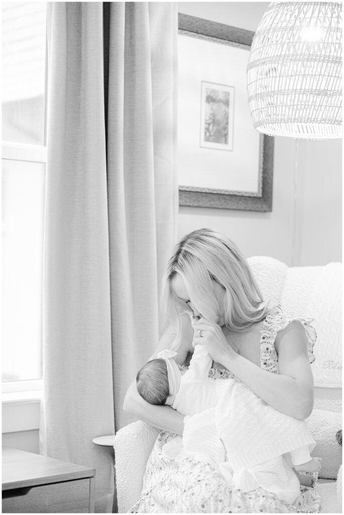 In a black and white photo, mom gently kisses her baby's hand during their newborn session in Northern Virginia.