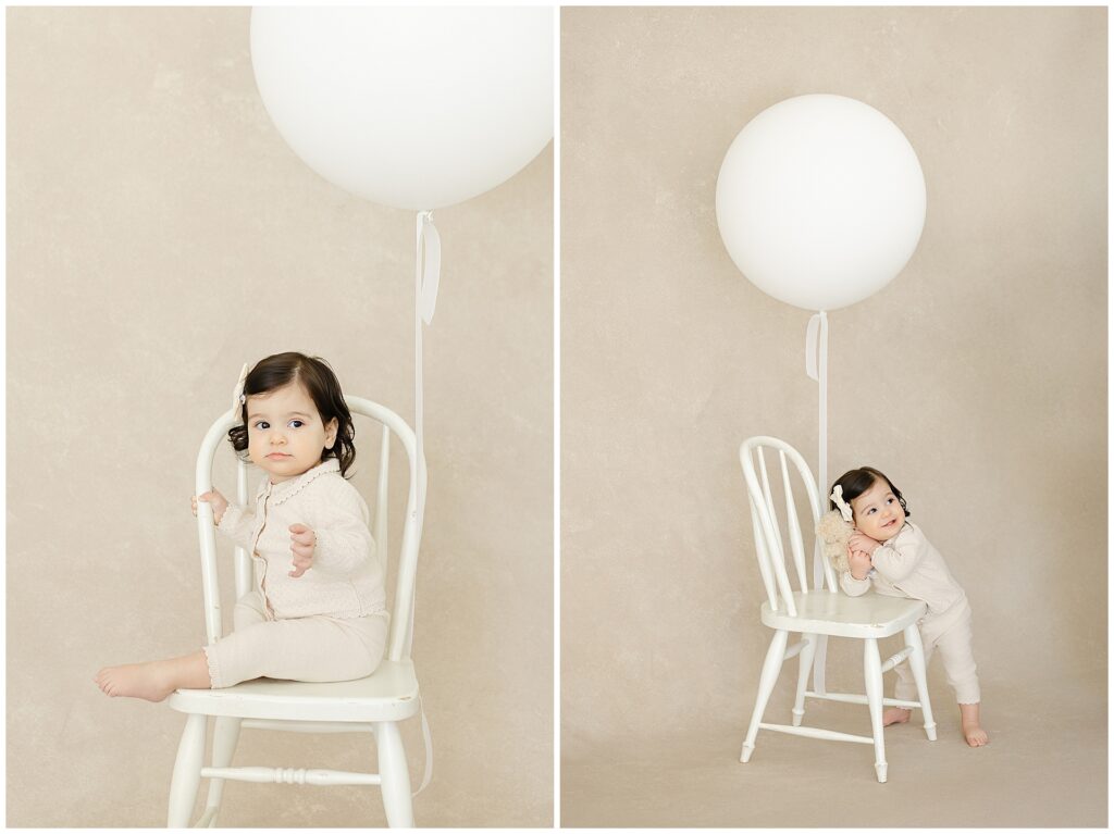 Heirloom-style first birthday portrait of a one-year-old girl seated on a white chair with a white balloon against a hand-painted backdrop during first birthday photos in Annapolis