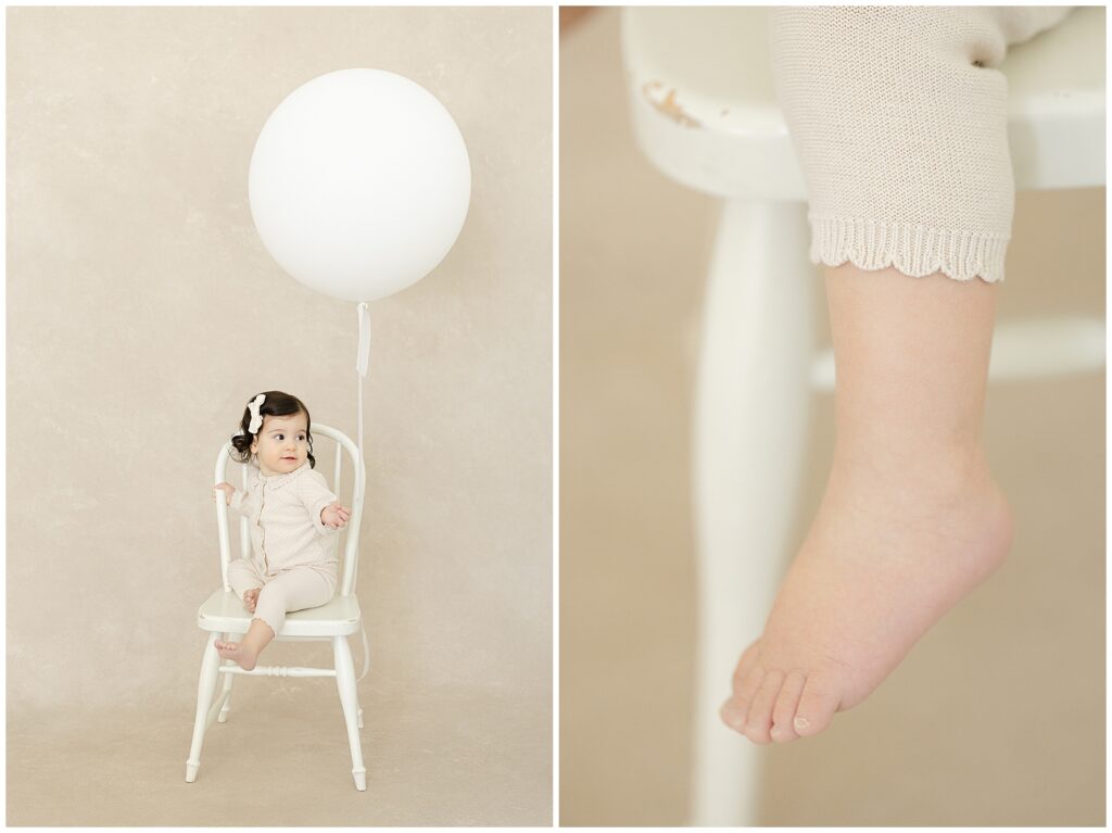 Heirloom-style first birthday portrait of a one-year-old girl seated on a white chair with a white balloon against a hand-painted backdrop during first birthday photos in Annapolis