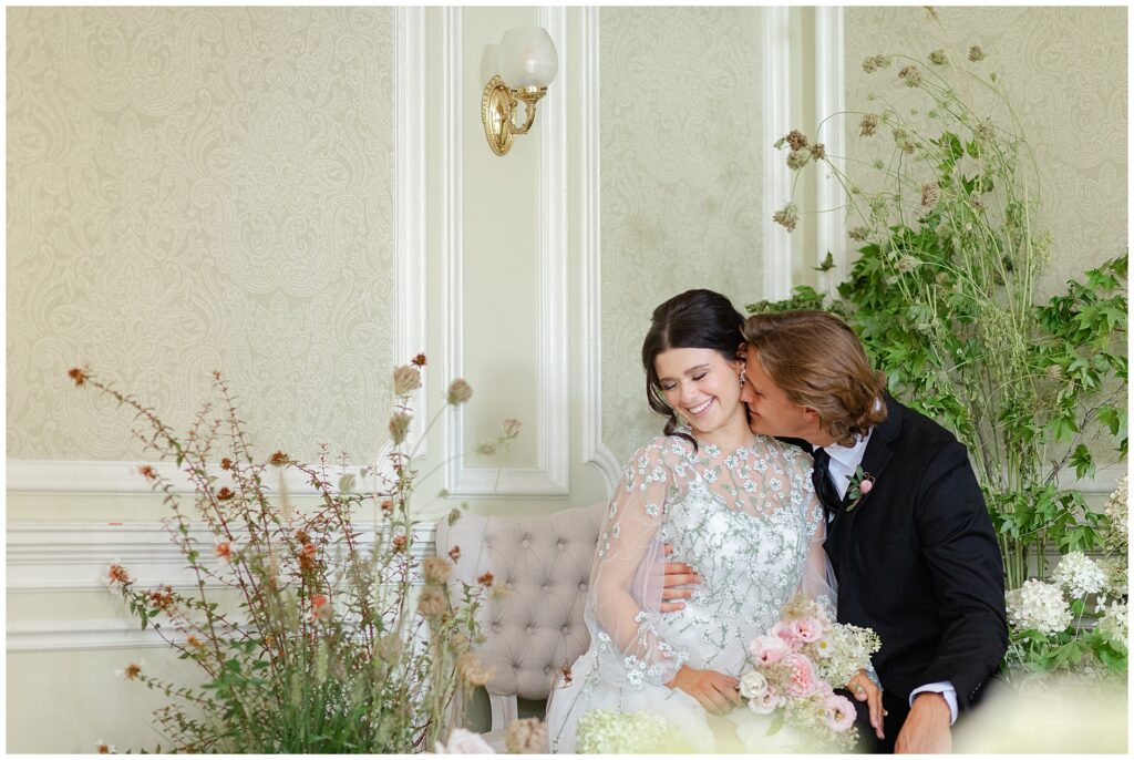 Intimate wedding portrait of a couple cuddling on a sofa inside the Dining Room at Cairnwood Estate, with the groom kissing the bride’s neck in a quiet, romantic moment. The image captures emotional connection and timeless interior portraits at a historic Pennsylvania estate wedding venue near Philadelphia.