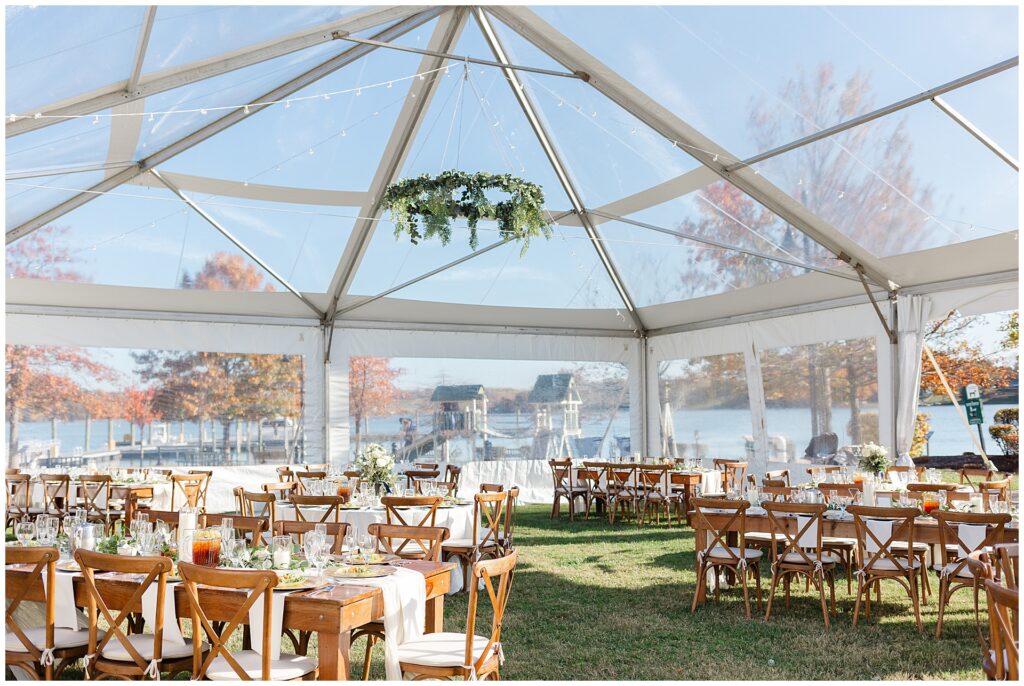 a clear top tent with clear sidewalls featuring farm tables with hanging greenery, overlooking the Potomac river at a Maryland waterfront wedding