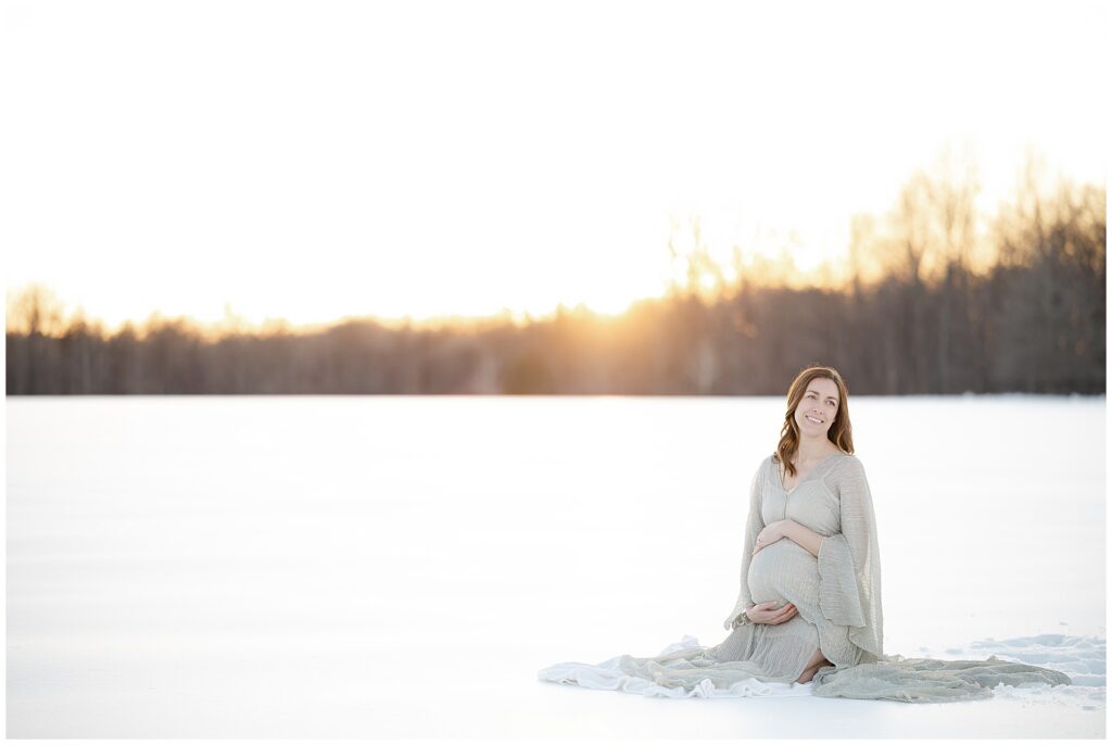 Pregnant woman sitting in the snow looking off to the side during her snow maternity session in Maryland