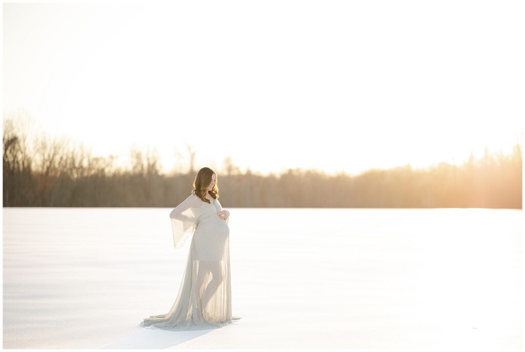 Woman in a silver dress stands in a field of snow in Howard County Maryland at golden hour