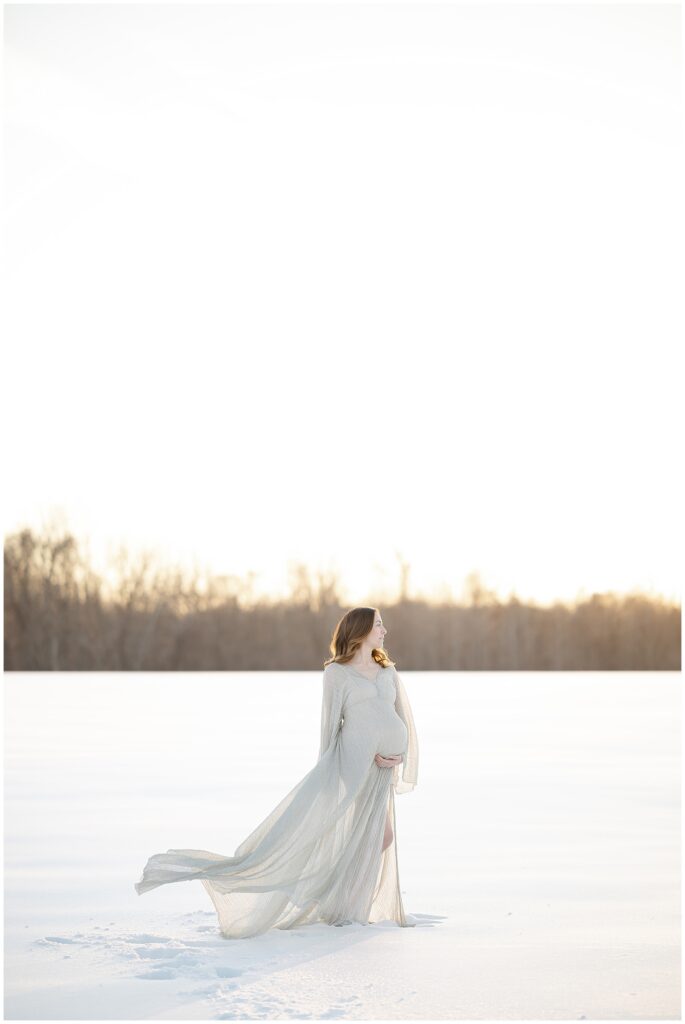 Fine art maternity photo of a woman in a silver dress, cradling her bump in her snow maternity session in maryland