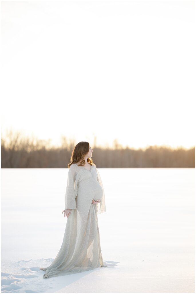 Fine art maternity photo of a woman in a silver dress, cradling her bump in her snow maternity session in maryland