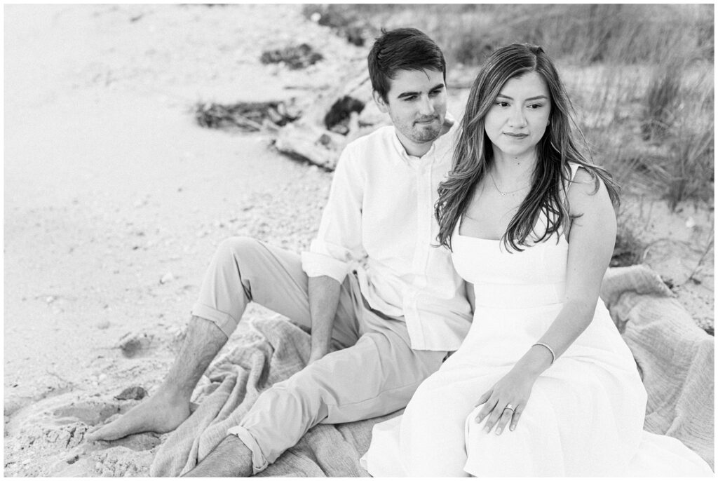 Couple sitting on the beach during their soft coastal setting during a Maryland beach engagement session.