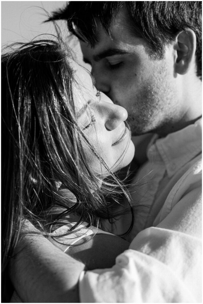 Editorial maryland beach engagement session, direct sun lighting the womans face as the man in the background kisses her cheek