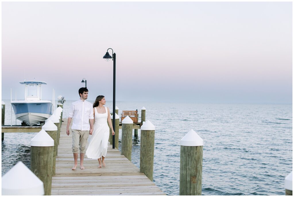 Blue hour photo of couple walking down a pier with the faint color in the clouds